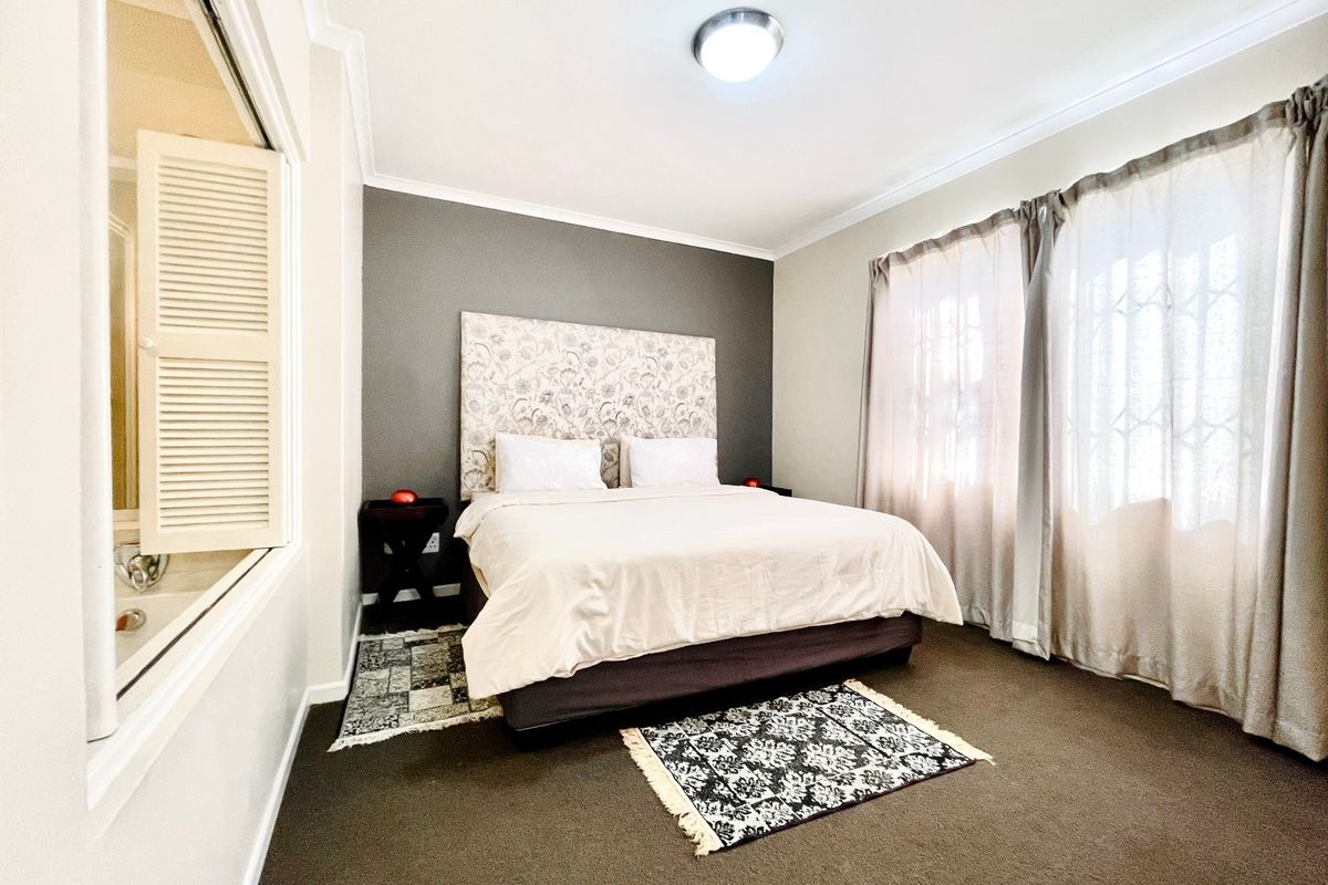 A well-maintained bedroom featuring dark carpeting, a feature wall, and an internal window with shutters looking into the adjacent bathroom area.