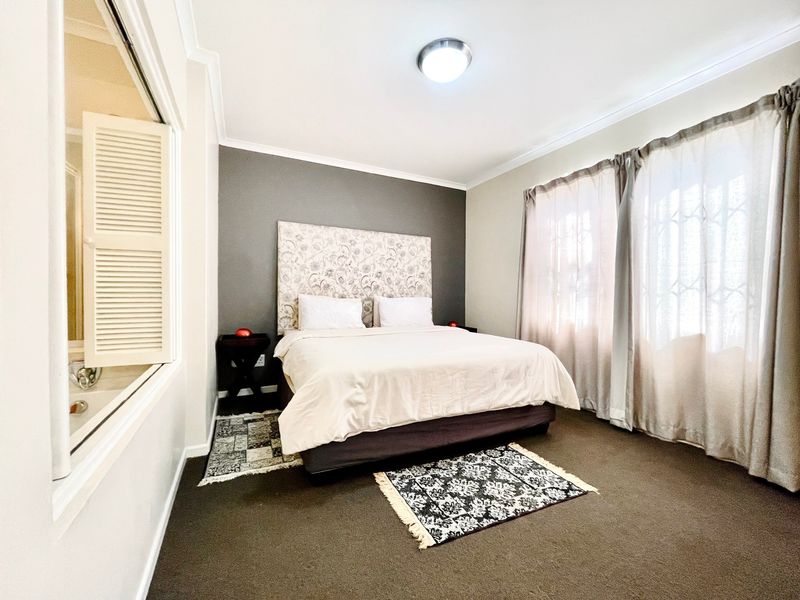 A well-maintained bedroom featuring dark carpeting, a feature wall, and an internal window with shutters looking into the adjacent bathroom area.