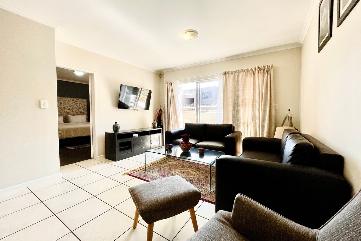 A bright living room featuring tiled flooring and a sliding glass door providing access to the exterior, with a view into the adjacent bedroom.