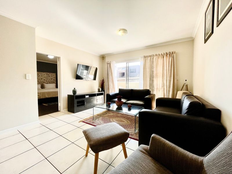 A bright living room featuring tiled flooring and a sliding glass door providing access to the exterior, with a view into the adjacent bedroom.