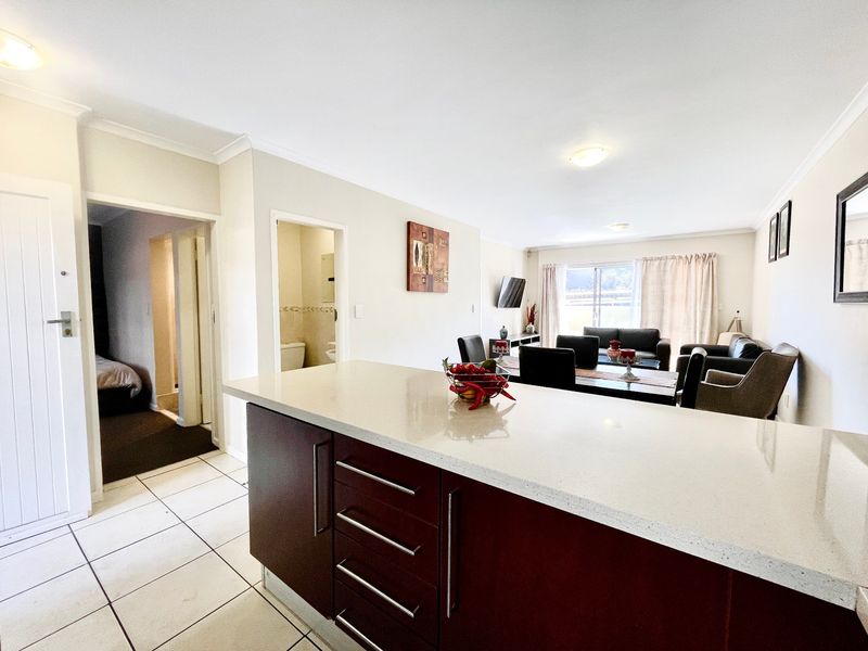 Open plan living and dining area featuring a modern kitchen island with stone countertops and tiled flooring, flowing into a comfortable lounge space.