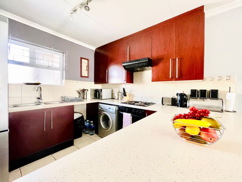 Functional kitchen featuring dark wood-finish cabinetry, light countertops, tiled backsplash, and integrated appliances including an electric hob and oven.