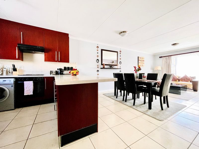 Open-plan living and dining area featuring a modern kitchen with dark cabinetry, breakfast bar, and tiled flooring throughout.