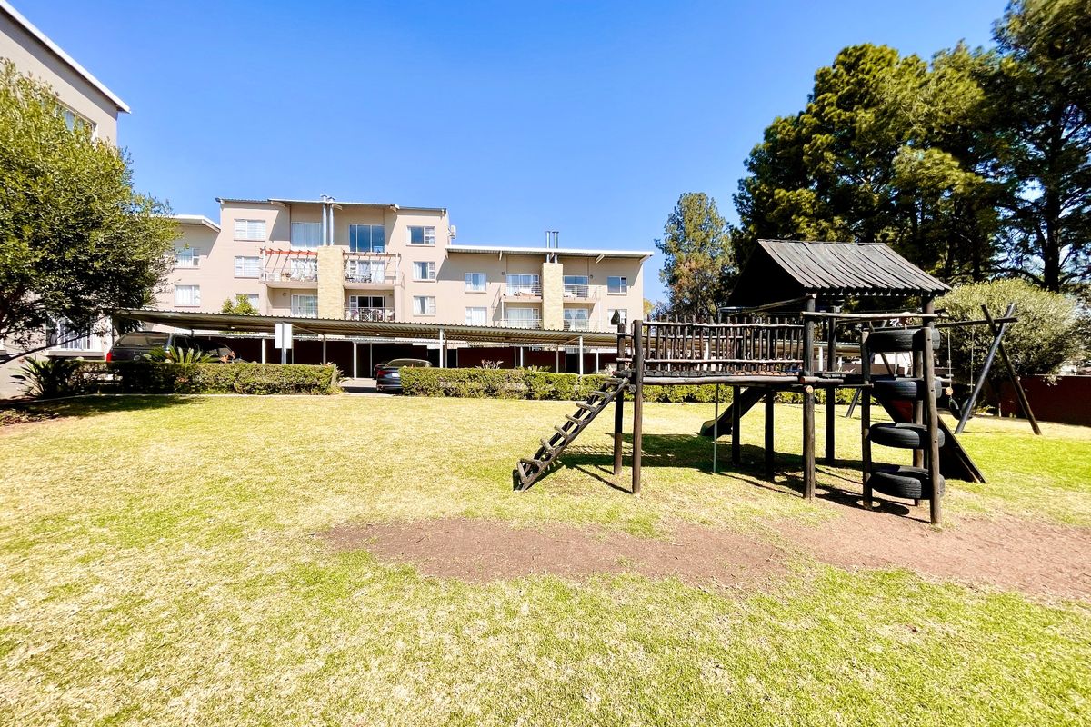 Communal garden area featuring a children's playground structure and covered parking bays for residents within the apartment complex.
