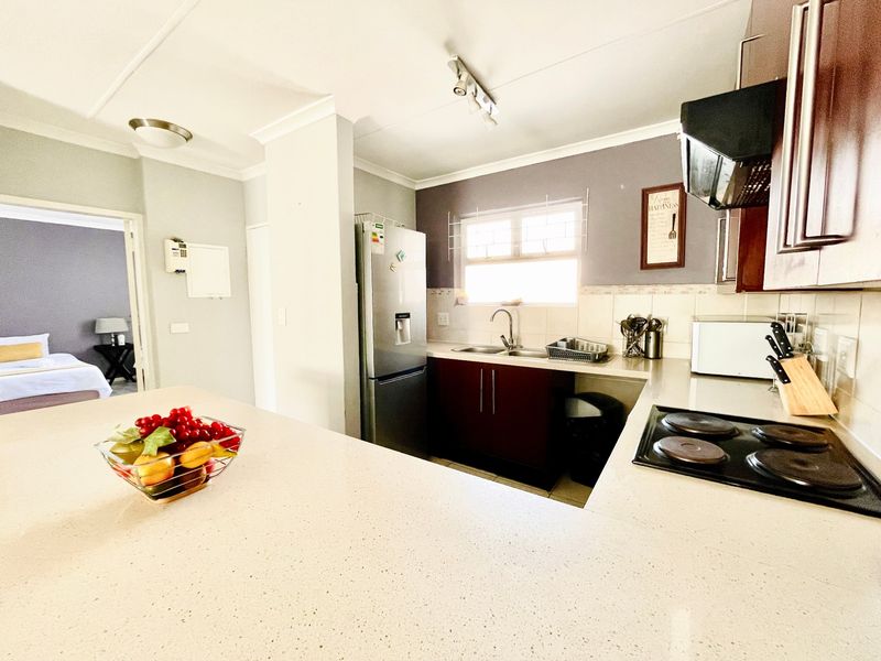 A functional kitchen featuring dark cabinetry, stone countertops, an electric hob with extractor fan, and a double sink, with an open-plan layout.