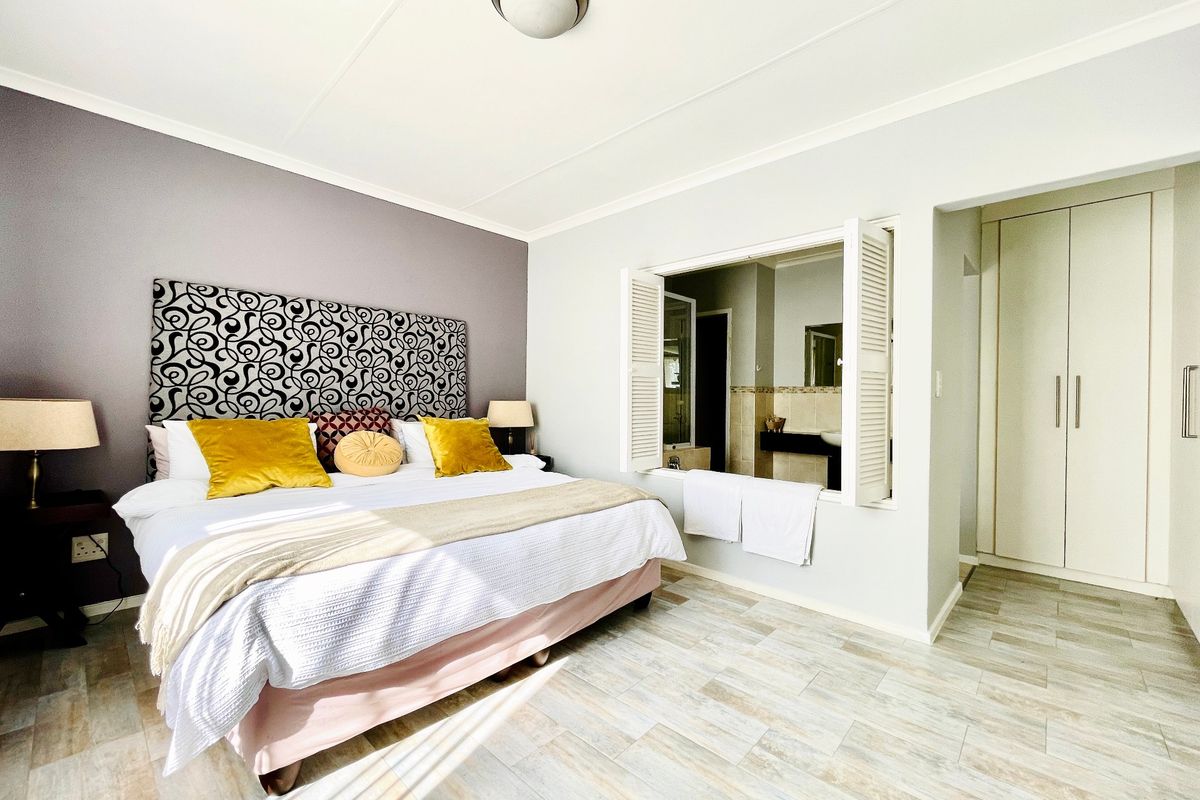 A well-maintained bedroom featuring tiled flooring, built-in cupboards, and a unique shuttered window opening into the adjacent bathroom.