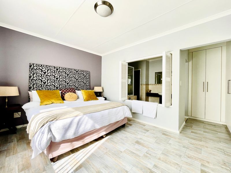 A well-maintained bedroom featuring tiled flooring, built-in cupboards, and a unique shuttered window opening into the adjacent bathroom.