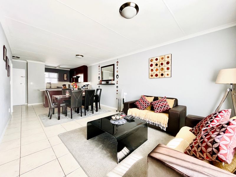 Open plan living and dining area featuring tiled flooring and a functional kitchen with dark cabinetry and a breakfast counter.