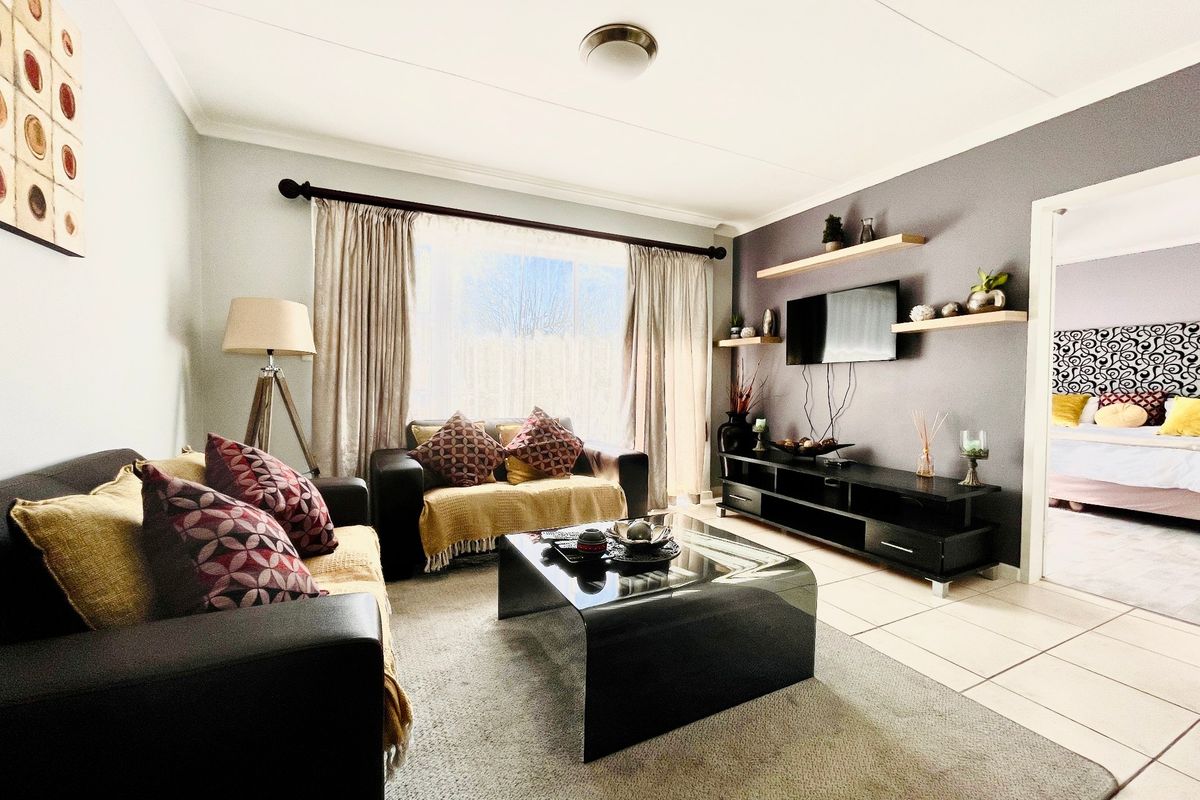 A well-maintained living room featuring tiled flooring, floating wall shelves, and a neutral color palette with a feature wall.