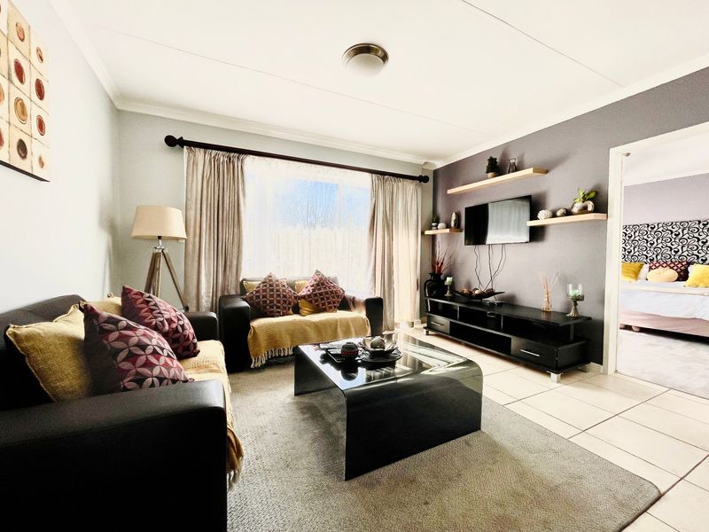 A well-maintained living room featuring tiled flooring, floating wall shelves, and a neutral color palette with a feature wall.