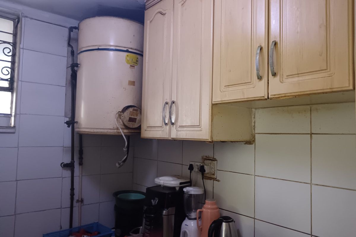 A dated kitchen area featuring wall-mounted cabinetry, ceramic tiling, and an exposed electric water heater unit.