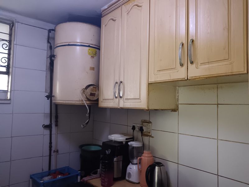 A dated kitchen area featuring wall-mounted cabinetry, ceramic tiling, and an exposed electric water heater unit.