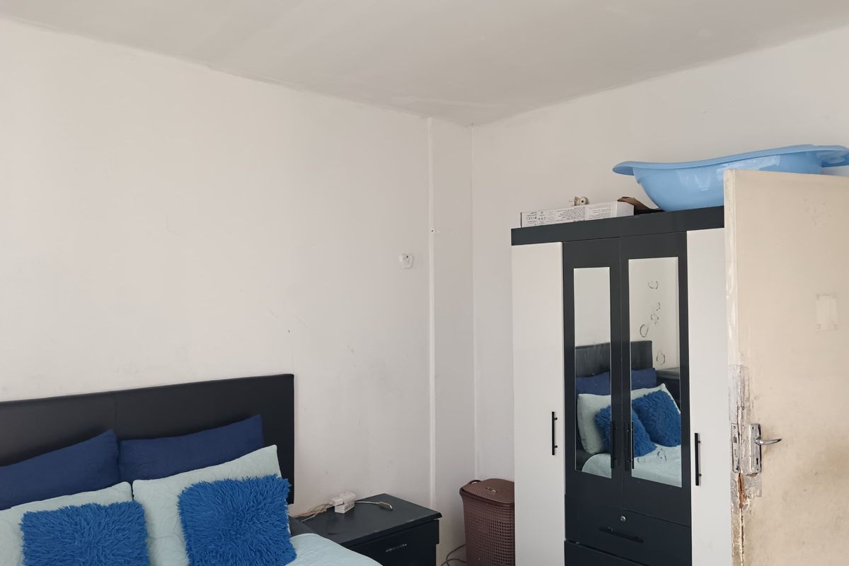 A bedroom featuring plain white walls and a standard door. The room shows signs of wear, particularly on the door frame.