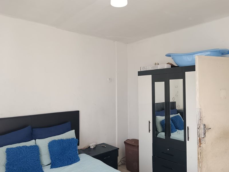 A bedroom featuring plain white walls and a standard door. The room shows signs of wear, particularly on the door frame.