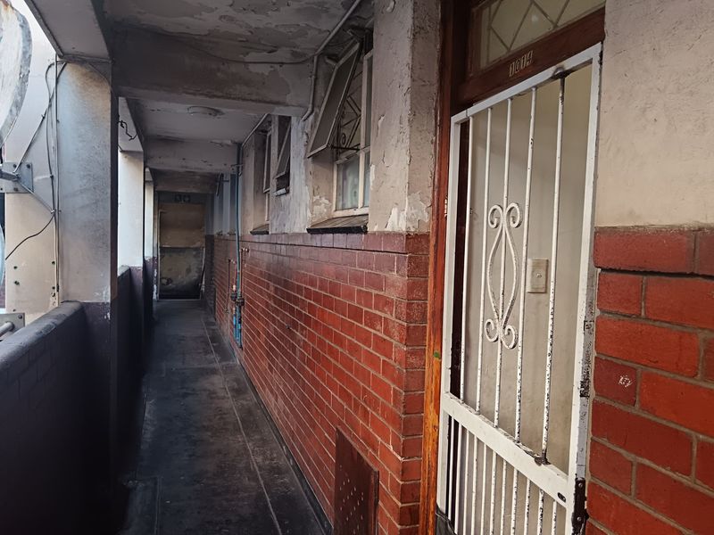 Exterior apartment hallway featuring brick walls, a security gate entrance, and visible signs of wear on the ceiling and wall finishes.