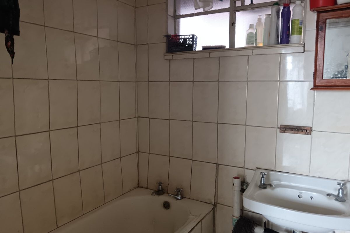 A dated bathroom featuring a bathtub, wall-mounted basin, and tiled walls. The space requires cosmetic updates to improve its overall condition and aesthetic appeal.