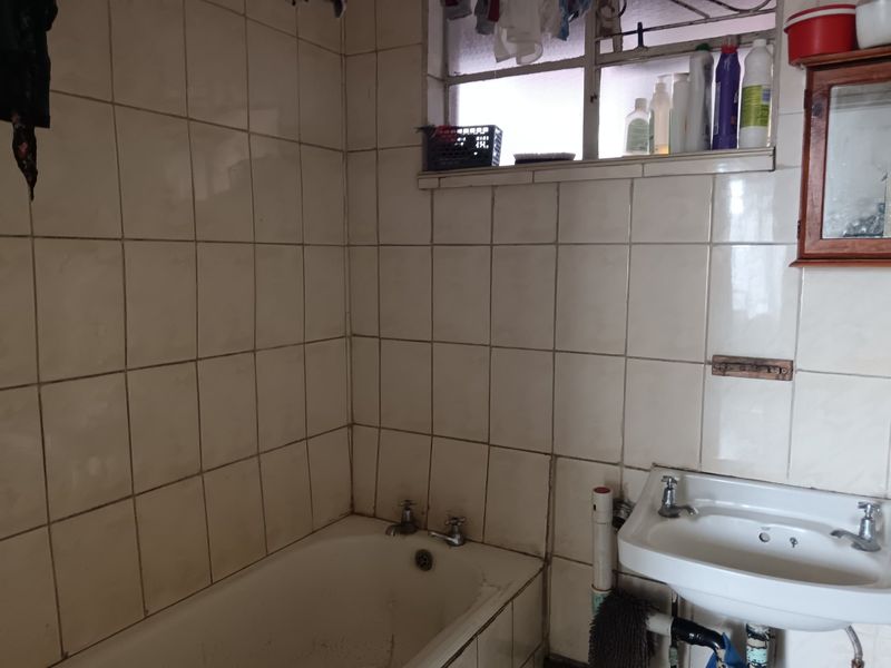 A dated bathroom featuring a bathtub, wall-mounted basin, and tiled walls. The space requires cosmetic updates to improve its overall condition and aesthetic appeal.