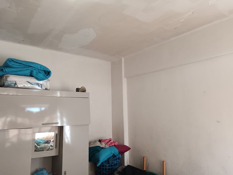 A bedroom interior featuring unfinished ceiling plaster and scuffed wall surfaces, requiring cosmetic attention and painting to improve the overall condition.