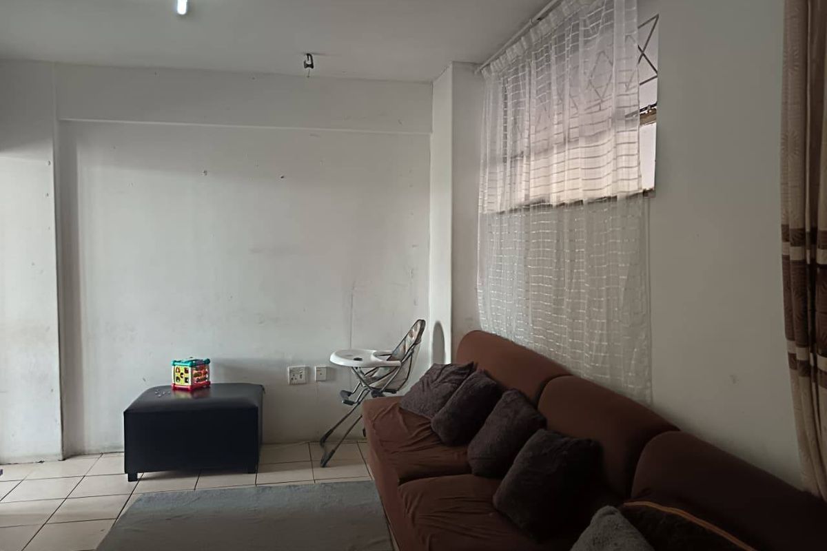 A living room area featuring tiled flooring and a window with security bars, requiring minor cosmetic updates to the walls and ceiling fixtures.