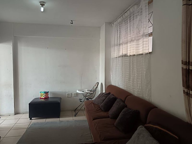 A living room area featuring tiled flooring and a window with security bars, requiring minor cosmetic updates to the walls and ceiling fixtures.