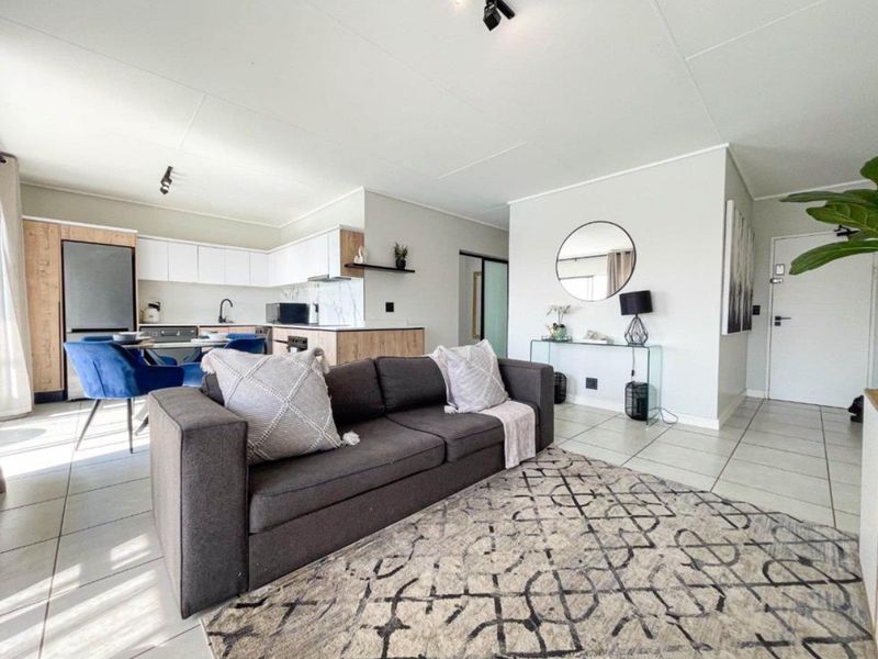 A bright open-plan living and kitchen area featuring modern cabinetry, tiled flooring, and a functional layout suitable for contemporary apartment living.