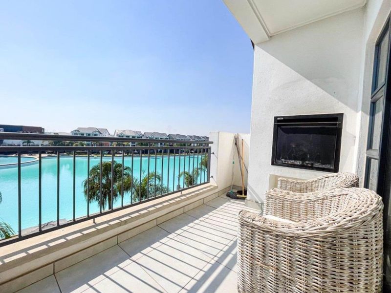 A spacious balcony featuring a built-in fireplace, metal balustrade, and tiled flooring, offering scenic views of the estate's lagoon.
