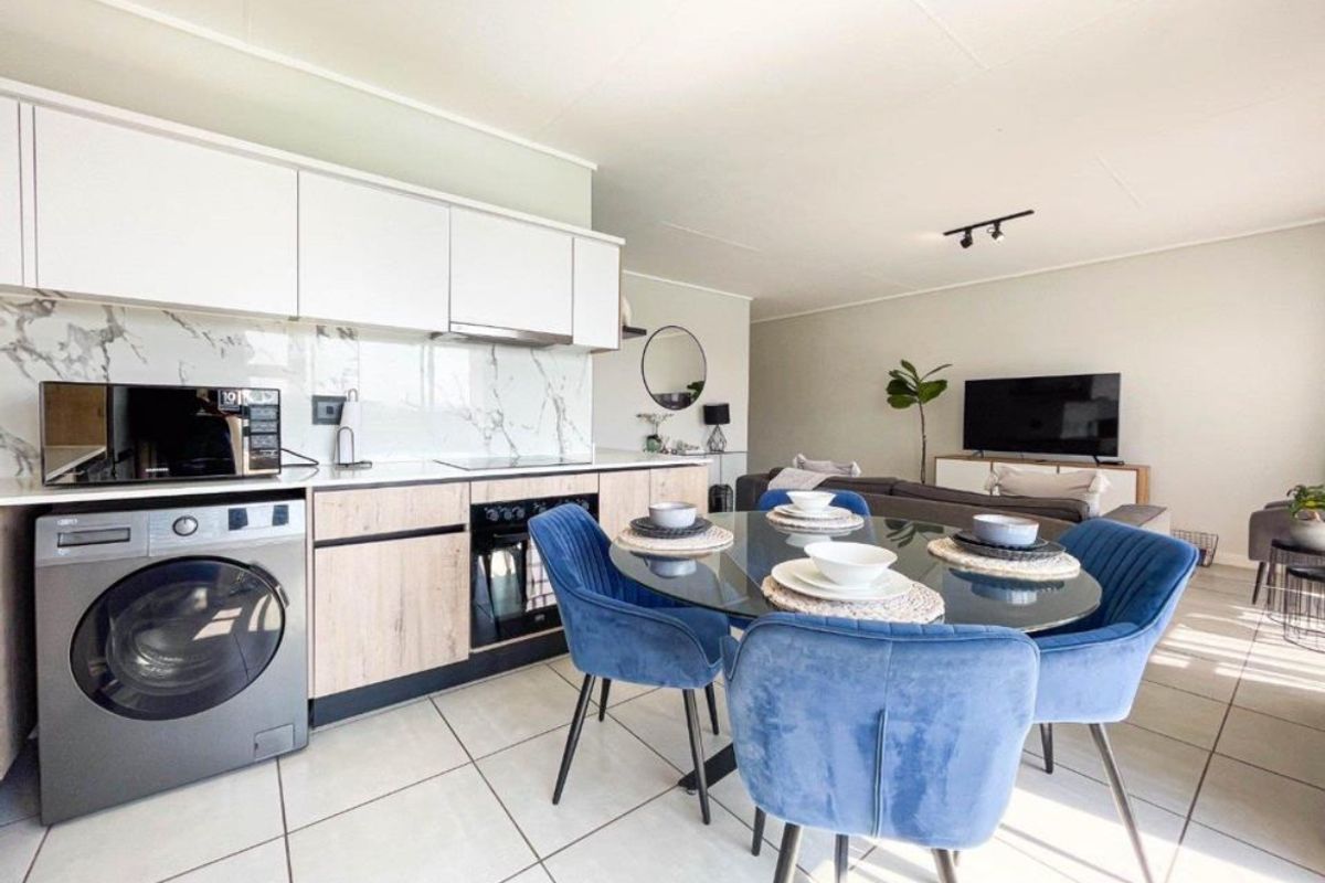 Modern open-plan living area featuring a contemporary kitchen with marble-look splashback, integrated appliances, and sleek cabinetry, flowing into a bright, tiled dining and lounge space.