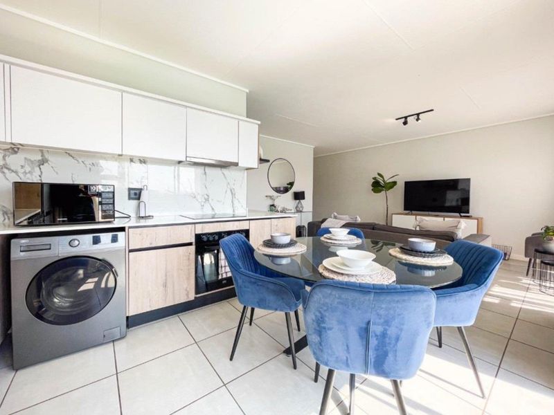 Modern open-plan living area featuring a contemporary kitchen with marble-look splashback, integrated appliances, and sleek cabinetry, flowing into a bright, tiled dining and lounge space.