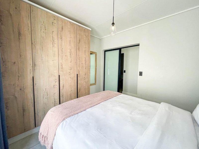 A well-maintained bedroom featuring modern wood-finish built-in cupboards, neutral walls, and a contemporary pendant light fixture.