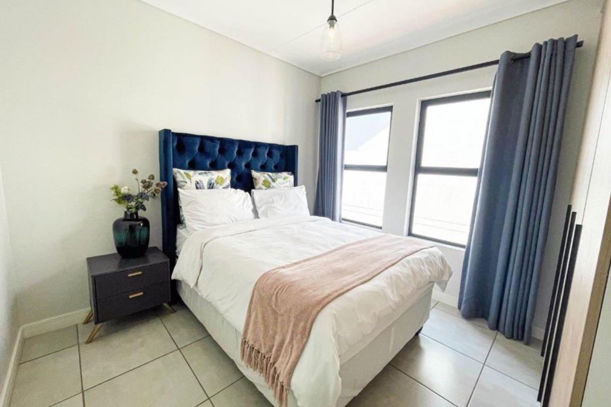 A well-maintained bedroom featuring neutral tiled flooring, built-in storage, and large windows with curtain rails, providing a bright and comfortable living space.