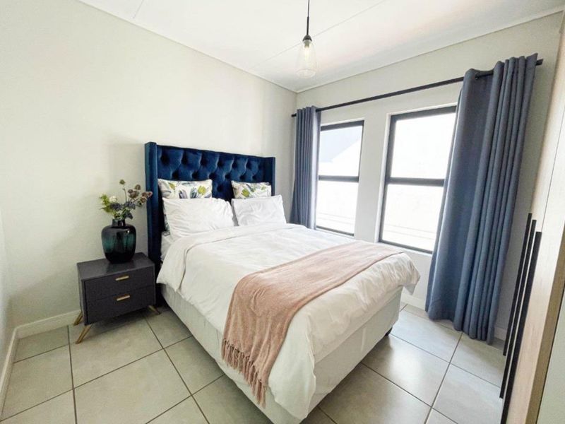 A well-maintained bedroom featuring neutral tiled flooring, built-in storage, and large windows with curtain rails, providing a bright and comfortable living space.
