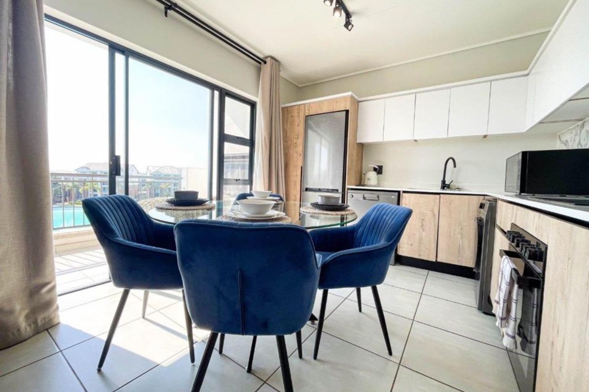 Modern open-plan kitchen and dining area featuring contemporary cabinetry, integrated appliances, tiled floors, and large sliding doors leading to a balcony.