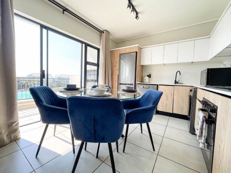 Modern open-plan kitchen and dining area featuring contemporary cabinetry, integrated appliances, tiled floors, and large sliding doors leading to a balcony.