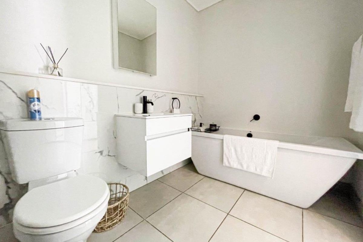 Modern bathroom featuring a sleek freestanding bathtub, wall-mounted vanity, marble-look wall tiling, and contemporary black matte fixtures.