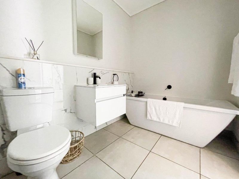 Modern bathroom featuring a sleek freestanding bathtub, wall-mounted vanity, marble-look wall tiling, and contemporary black matte fixtures.