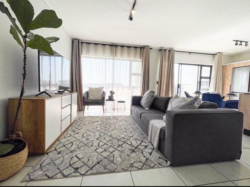 A bright open-plan living area featuring tiled flooring, modern track lighting, and large sliding glass doors that provide ample natural light.