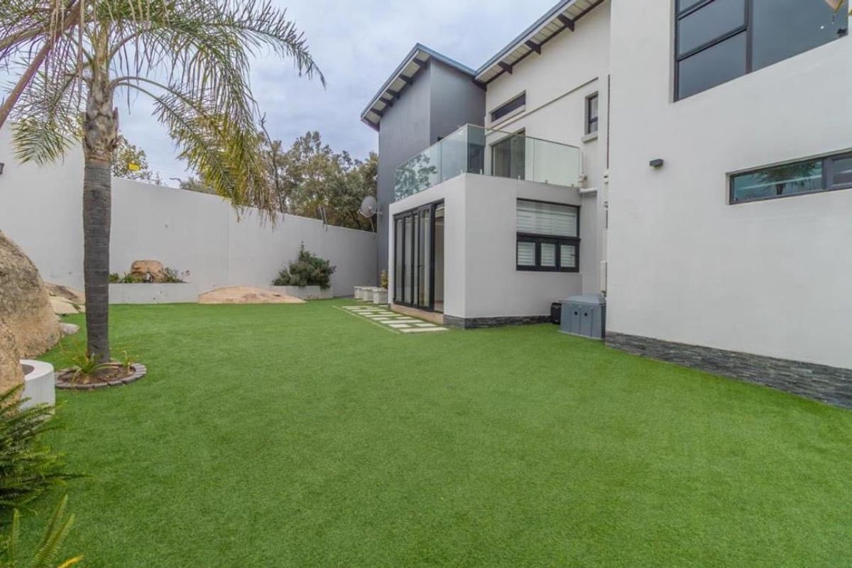A well-maintained rear garden featuring artificial turf, stone cladding accents, and a modern balcony with a glass balustrade.
