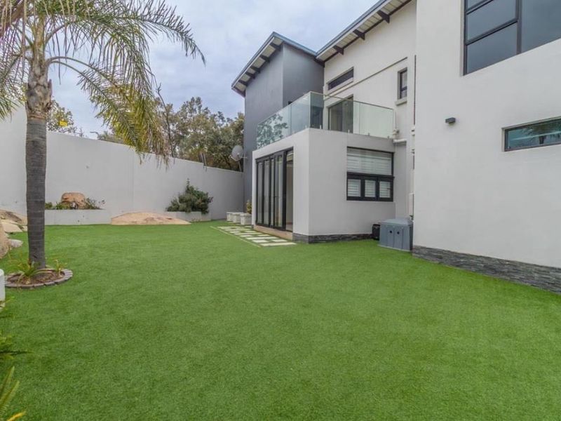 A well-maintained rear garden featuring artificial turf, stone cladding accents, and a modern balcony with a glass balustrade.