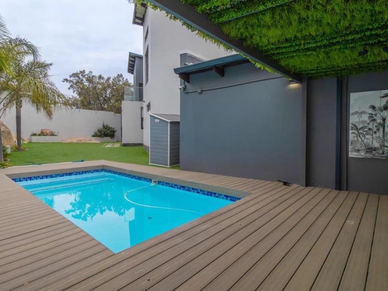 Modern outdoor entertainment area featuring a swimming pool, composite decking, and a covered pergola, set within a landscaped garden with boundary walls.