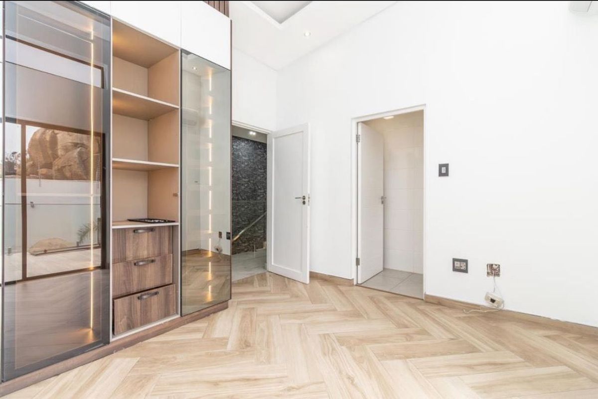 A modern bedroom featuring light herringbone flooring, built-in cabinetry with integrated lighting, and clean white finishes.