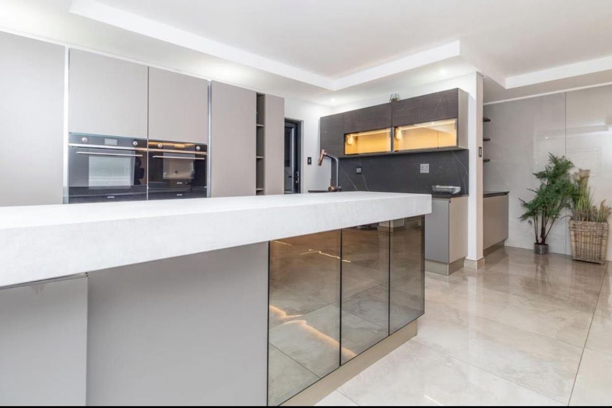 A modern, high-end kitchen featuring a large central island, sleek cabinetry, built-in double ovens, and polished tiled flooring with integrated lighting.