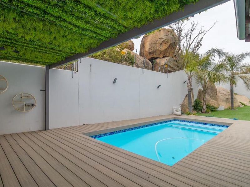 Outdoor pool area featuring composite decking, a covered pergola, artificial lawn, and a secure boundary wall with electric fencing.