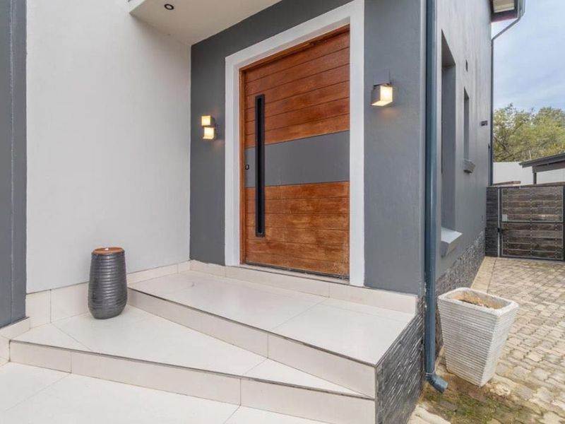 Modern front entrance featuring a contemporary timber door, tiled steps, and stylish exterior wall lighting, set against a clean, well-maintained facade.