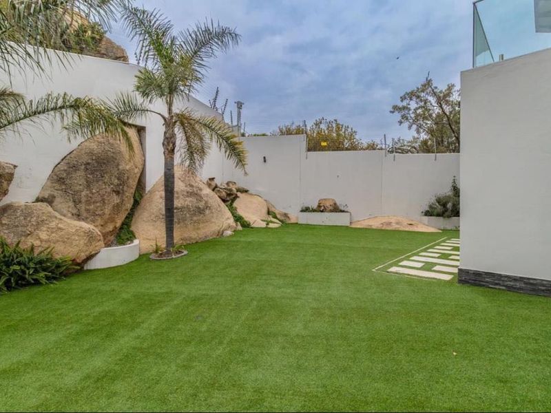 A well-maintained garden area featuring artificial turf, integrated natural rock landscaping, and clean perimeter walls.