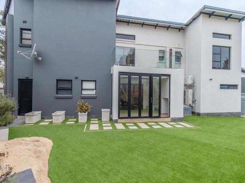 Modern rear elevation featuring bi-fold doors opening to a landscaped garden with artificial turf and a glass-balustraded balcony above.