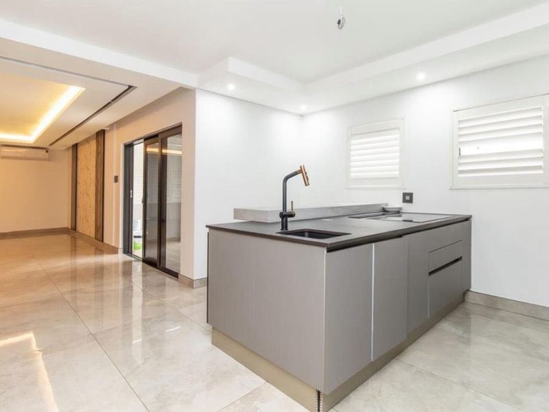 A modern, minimalist kitchen island featuring a sleek dark countertop, integrated sink, and built-in cooktop, set within a bright, open-plan living space.