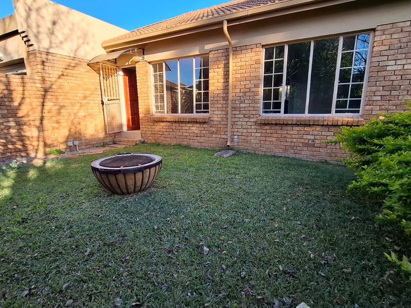A private rear garden area featuring a face brick townhouse facade, tiled roof, and established lawn.