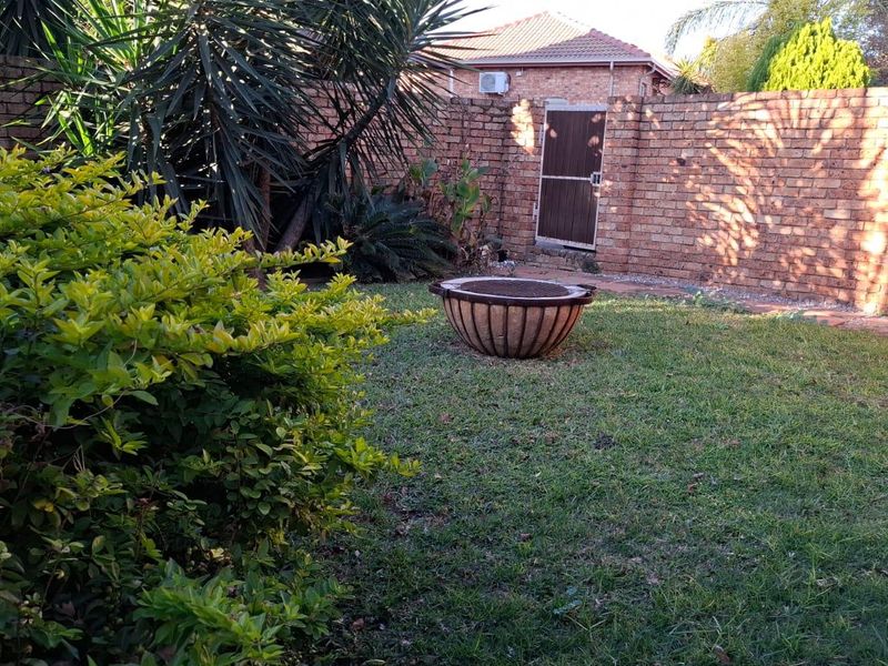 A private rear garden featuring a lawn area, established landscaping, and a brick boundary wall with a secure access gate.