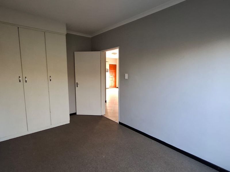 A clean, empty bedroom featuring neutral grey walls, carpeted flooring, and built-in storage cupboards.
