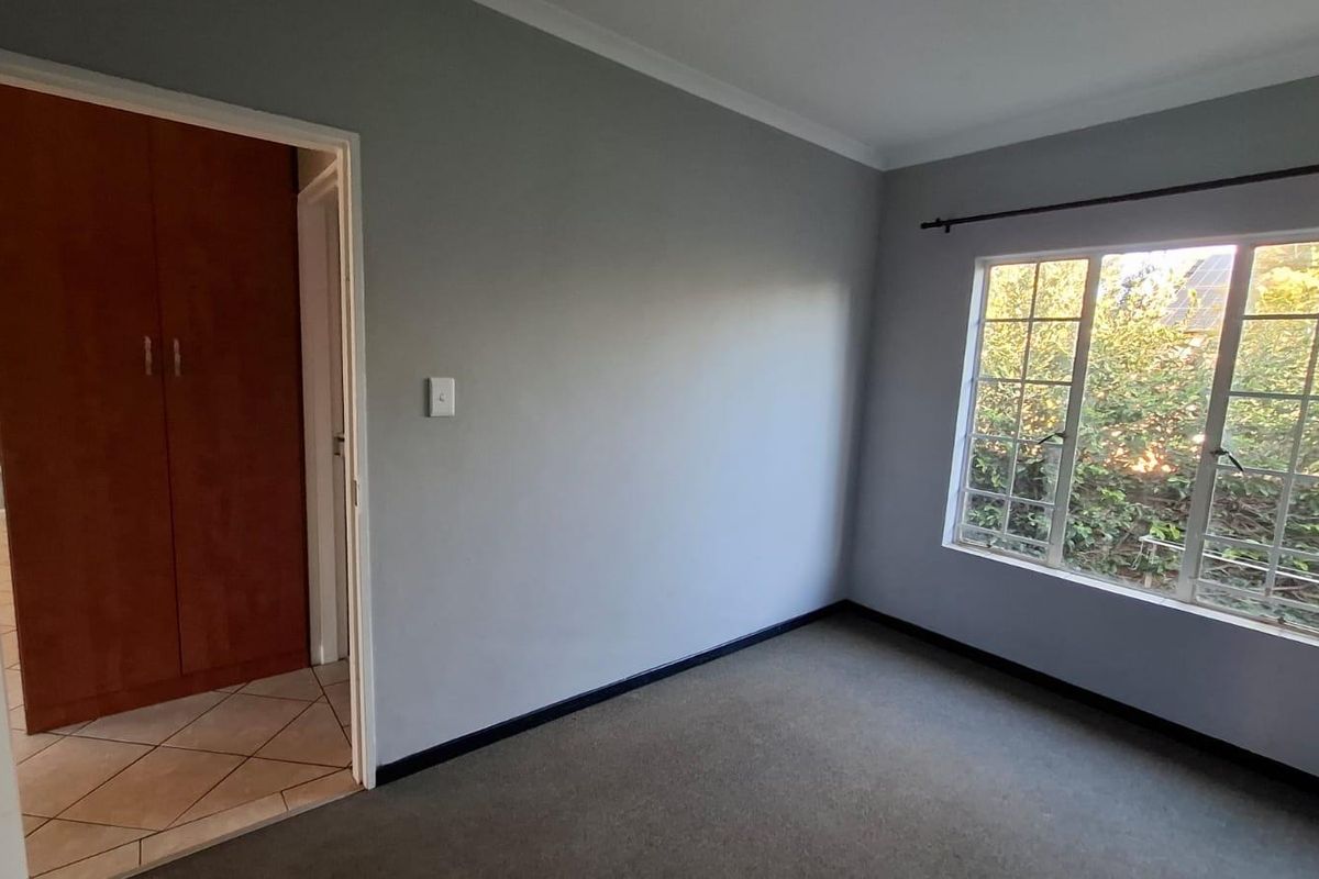 A vacant bedroom featuring grey walls, carpeted flooring, and built-in wooden cupboards, with natural light entering through a window with security bars.
